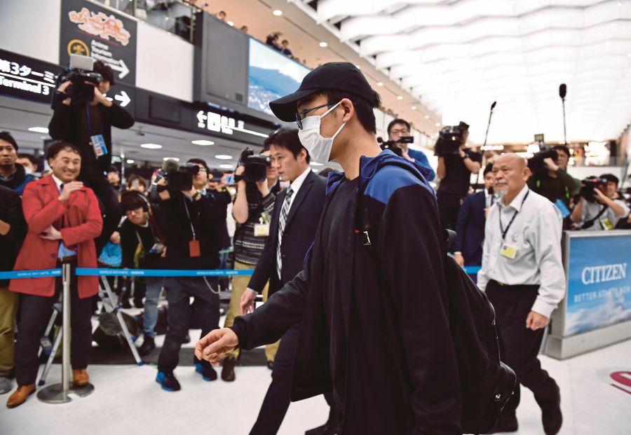 Kento Momota (centre) arriving at Narita Airport in Chiba yesterday after being released from a Malaysian hospital following a car crash that killed his driver and left him with minor injuries. -AFP
