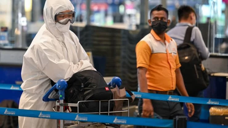 A passenger (L) wearing personal protective equipment (PPE) queues to check-in for a flight at the Kuala Lumpur International Airport (KLIA) in Sepang on November 29, 2021.