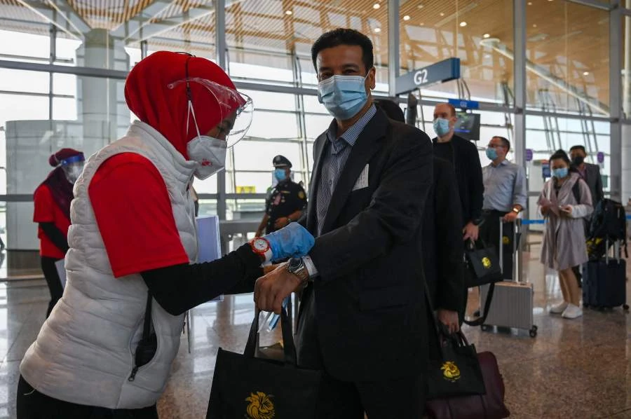 A health officer (L) installs a ribbon to a passenger after disembarking from Singapore Airlines aircraft after it landed in KLIA in Sepang, under the vaccinated travel lane for border crossing passengers in Sepang. - AFP Pic